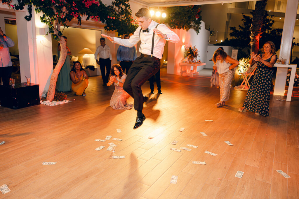 Man in formal attire jumping over scattered money on a decorated indoor event floor.