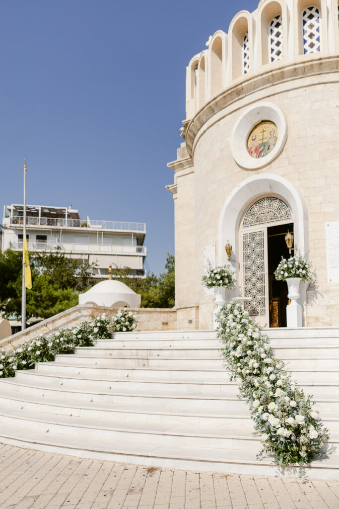 Stone building entrance with white floral arrangements along steps and ornate door under clear sky.