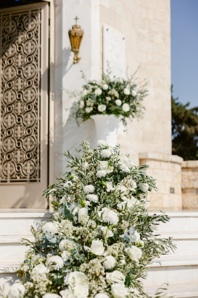 Marble steps leading to ornate door decorated with white flowers and green foliage arrangements.