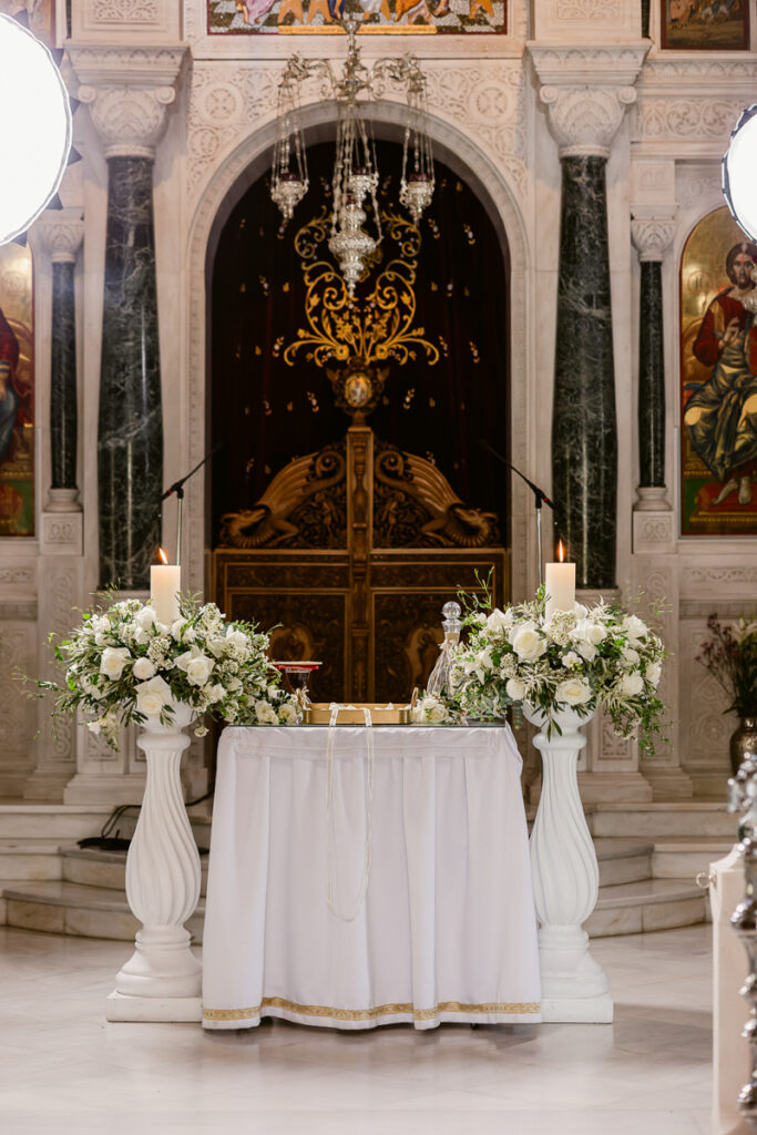 Church altar with white floral arrangements, lit candles, ornate doors, and religious paintings.