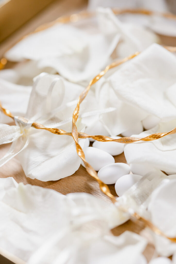 White sugared almonds on wooden surface with white fabric, bows, and twisted golden ribbon.