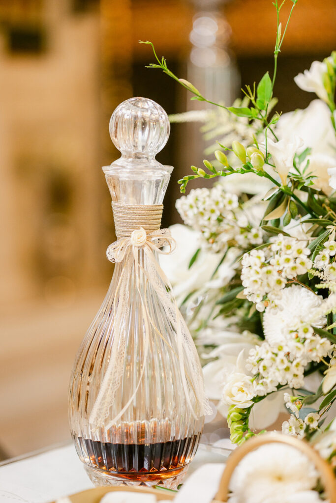 Ribbed glass decanter with round stopper and decorative ribbon, partially filled with dark liquid.