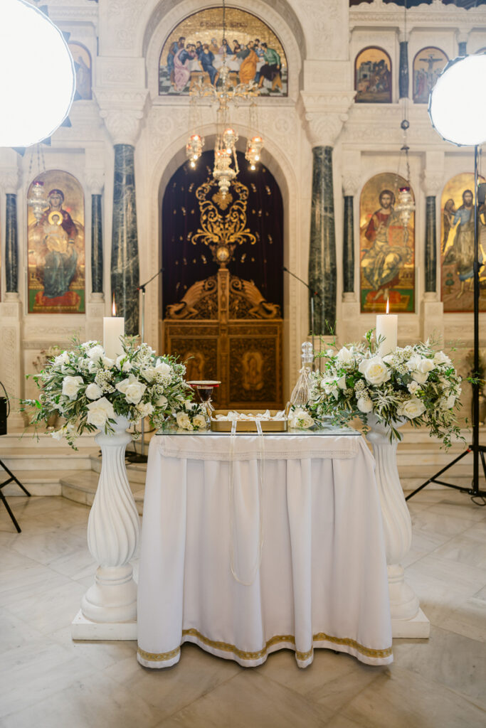Church altar with white floral arrangements, lit candles, religious icons, and ornate decorations.