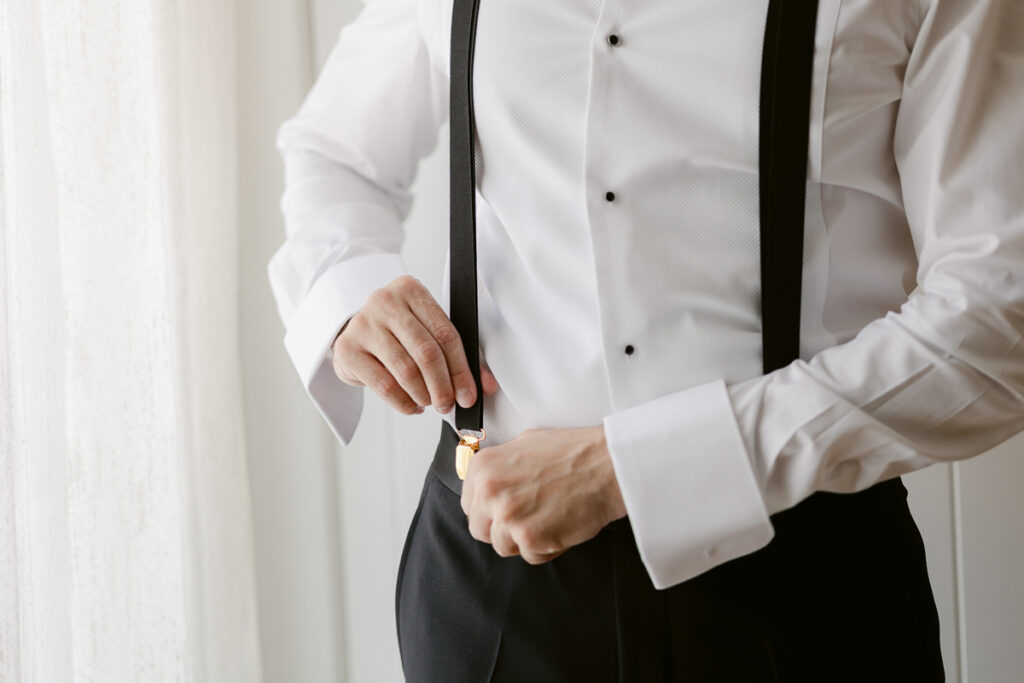 Person adjusting black suspenders over white dress shirt with black buttons and black pants.
