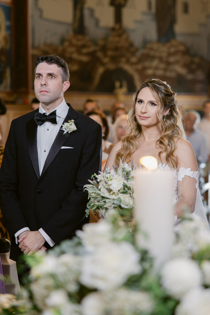 Bride and groom standing together at wedding ceremony holding bouquet and wearing formal attire.