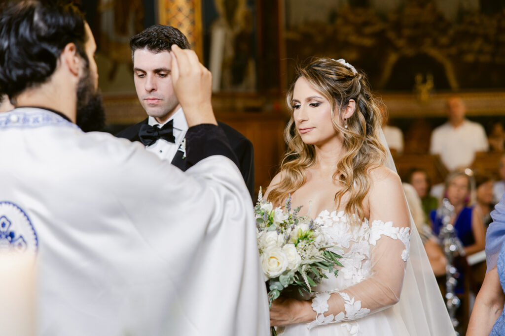 Bride and groom stand before priest during wedding ceremony inside decorated church.