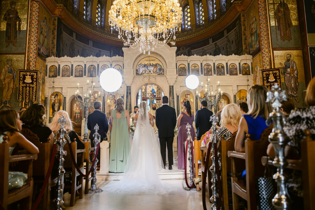 Wedding ceremony inside ornate church with bride, groom, wedding party, priest, and seated guests.