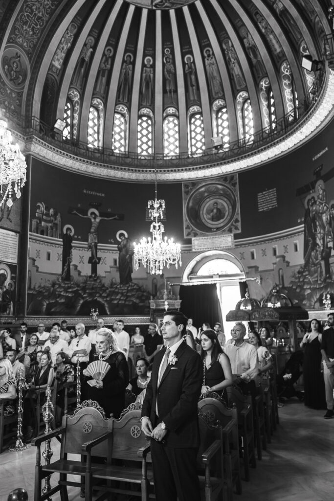 Black and white photo of people gathered inside a church with murals and chandeliers.