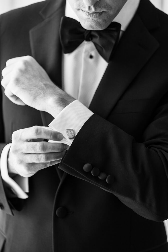 Man in a tuxedo adjusting cufflink on white dress shirt sleeve in black and white photo