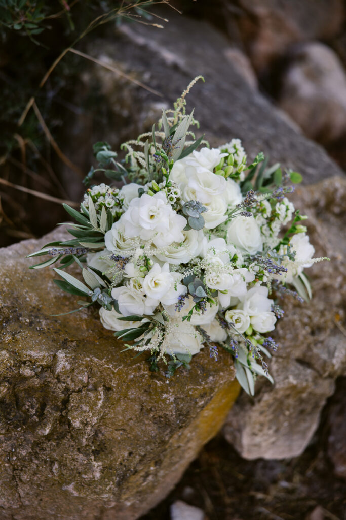 White flower bouquet with green leaves placed on a textured outdoor rock surface.