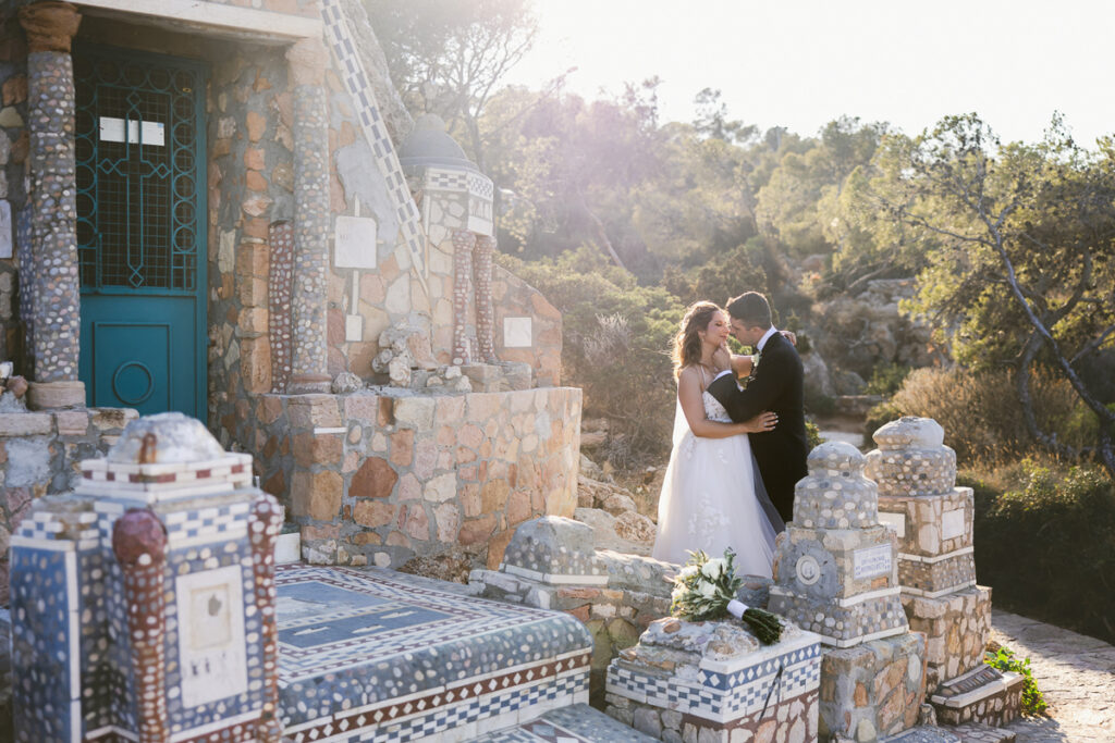 Bride and groom embracing near a stone mosaic structure with a blue door and bridal bouquet.