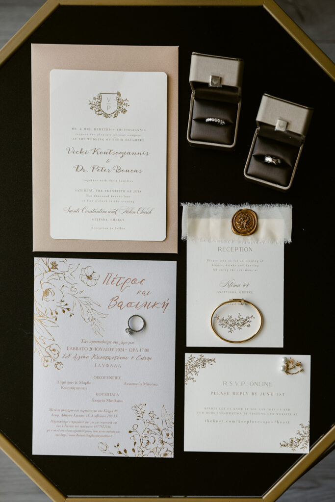 Wedding invitations, RSVP card, reception card, rings, earrings, and gold bracelet on black surface.