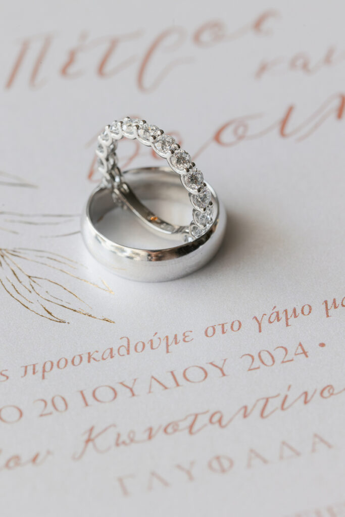 Two silver wedding rings on a Greek wedding invitation dated July 20, 2024.