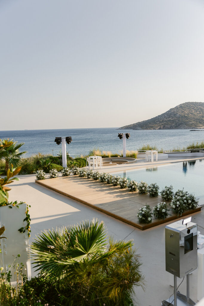 Outdoor waterfront venue with a wooden platform decorated with white flowers by the pool and sea.