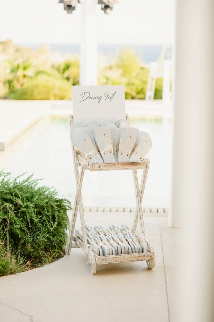 Wooden stand with white flip-flops and a sign reading Dancing Feet near a poolside.