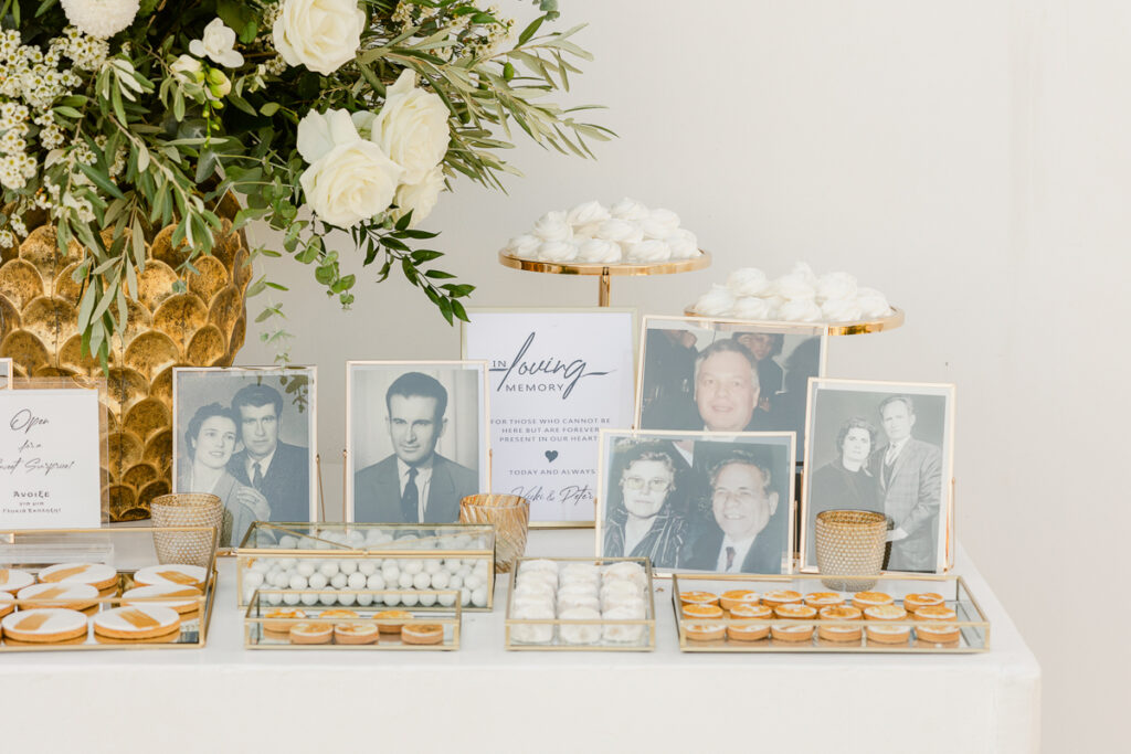 Memorial table with framed black-and-white photos, white cookies, meringues, and white roses.