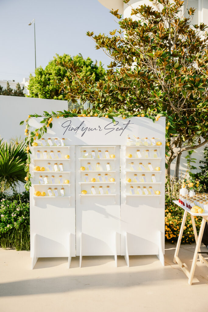 White seating board with Find your Seat text, cards on shelves, lemons, and lemon garland outdoors.