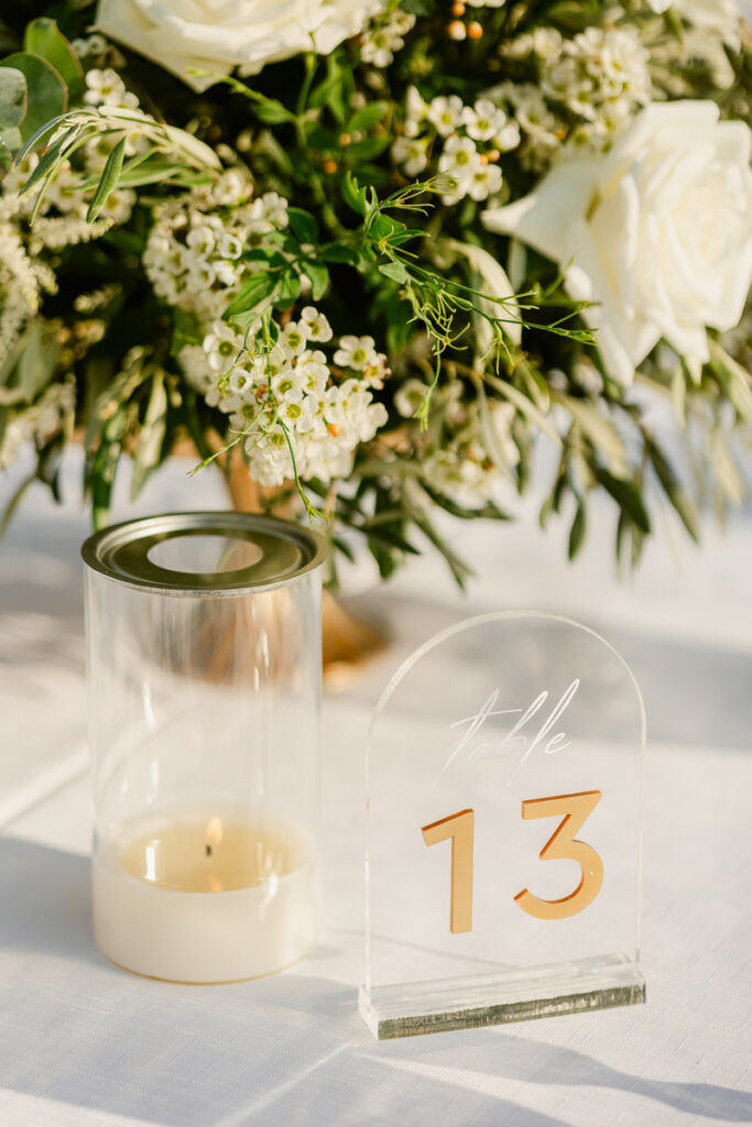 Clear acrylic table number 13 sign with a lit candle and white floral centerpiece on table.