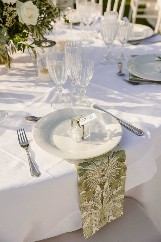 White plate with a small clear box of white candies and a green patterned napkin on a white tablecloth.