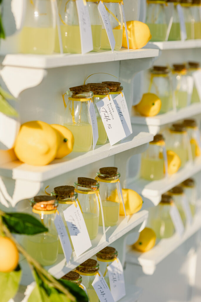 Glass jars of lemonade with cork lids and labels on white shelves alongside whole lemons.
