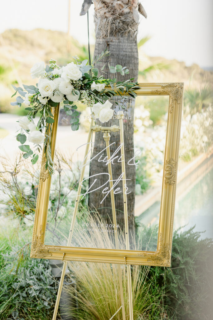Gold frame with white flowers and wedding details for Vicki and Peter, 20 July 2024, Athens Greece