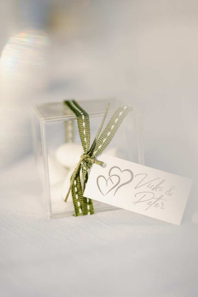 Transparent gift box with white almonds, green ribbon, and heart-themed name card.