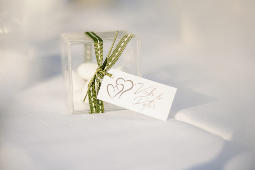 Clear plastic box with white candies, green ribbon, and a tag with hearts and names.