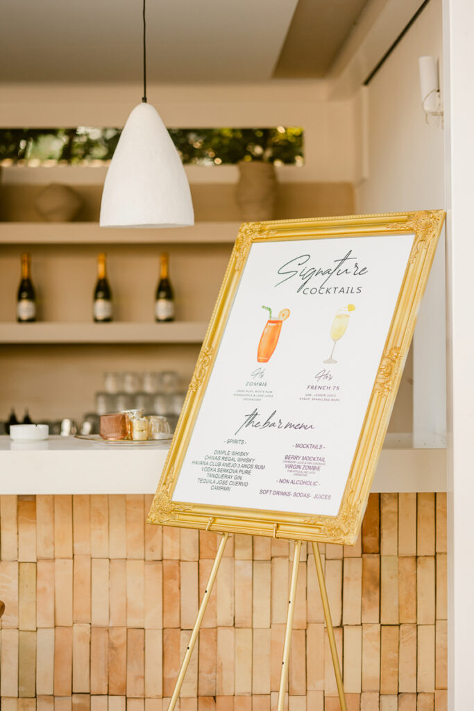Gold-framed easel menu displaying signature cocktails, spirits, mocktails, and non-alcoholic drinks.