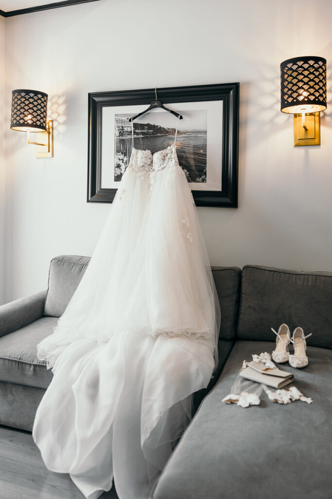White wedding dress hanging on a framed photo above a gray sofa with shoes and accessories.
